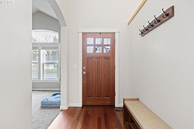 entryway featuring baseboards, arched walkways, and dark wood-type flooring