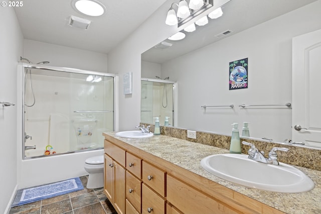 bathroom featuring double vanity, bath / shower combo with glass door, a sink, and toilet