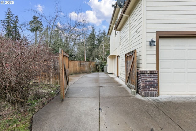 view of side of property with a garage, central air condition unit, fence, and brick siding