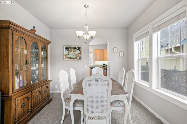 dining space featuring a chandelier, carpet, arched walkways, and baseboards