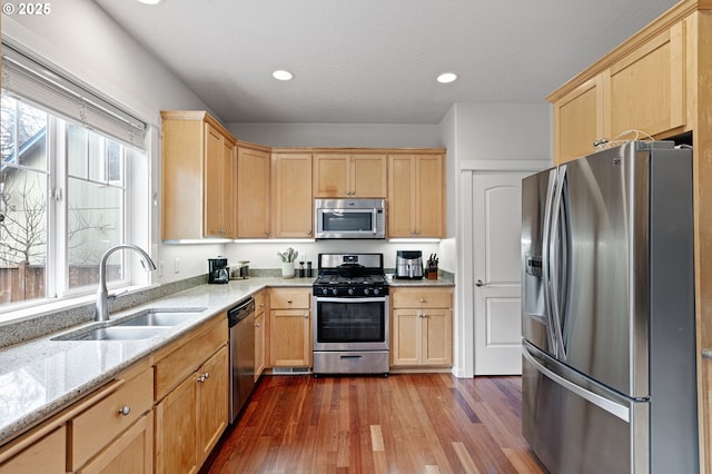 kitchen featuring dark wood-style floors, stainless steel appliances, light brown cabinets, a sink, and light stone countertops