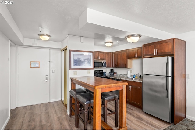 kitchen with sink, light hardwood / wood-style flooring, light stone countertops, and appliances with stainless steel finishes