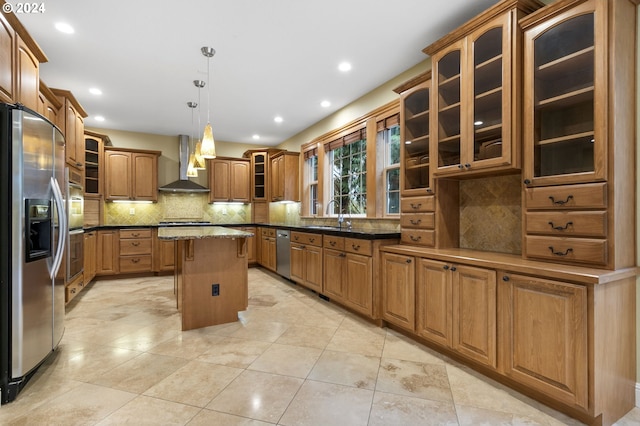 kitchen with wall chimney range hood, appliances with stainless steel finishes, pendant lighting, sink, and a center island