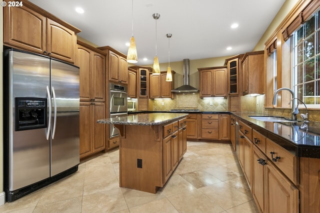 kitchen with stainless steel appliances, wall chimney range hood, hanging light fixtures, sink, and a center island