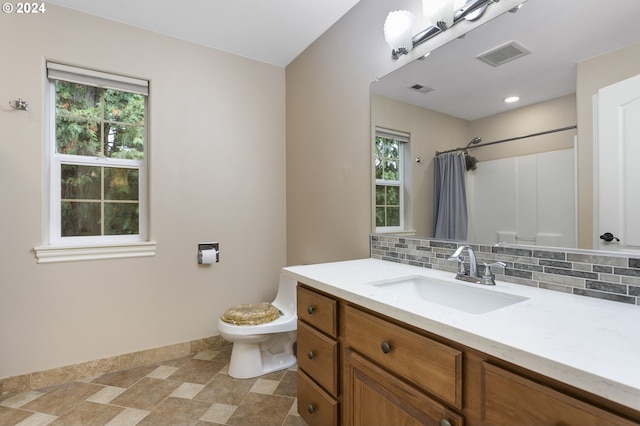 bathroom with a wealth of natural light, vanity, tasteful backsplash, and toilet