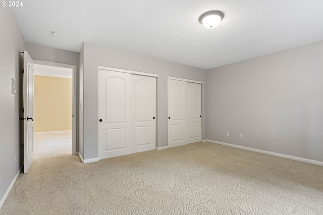 unfurnished bedroom featuring a textured ceiling, light carpet, and two closets