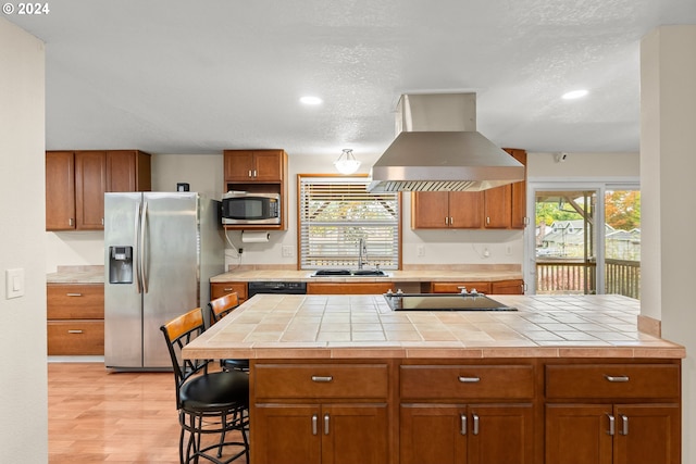 kitchen featuring sink, island exhaust hood, black appliances, tile countertops, and a wealth of natural light