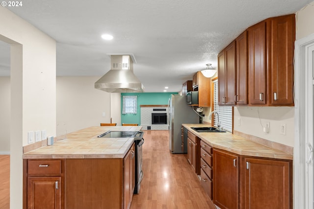 kitchen with wall chimney exhaust hood, sink, light hardwood / wood-style floors, tile countertops, and stainless steel electric range