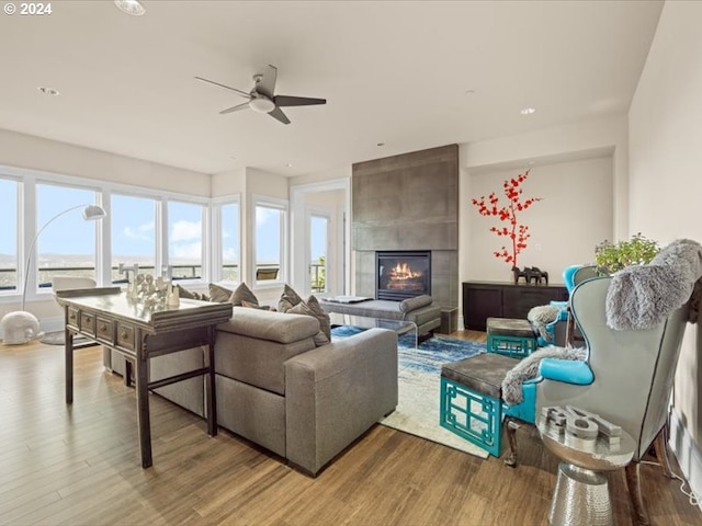 living area with a tile fireplace, ceiling fan, and wood finished floors