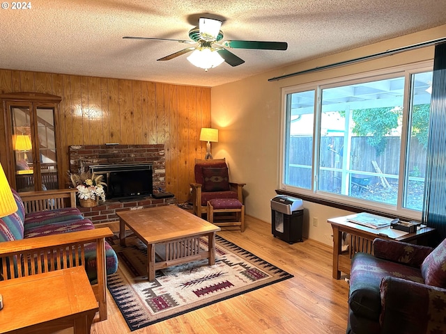 living room with a fireplace, a textured ceiling, wood walls, hardwood / wood-style floors, and ceiling fan