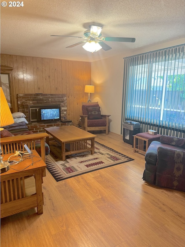 living room with light hardwood / wood-style floors, wood walls, a textured ceiling, and ceiling fan