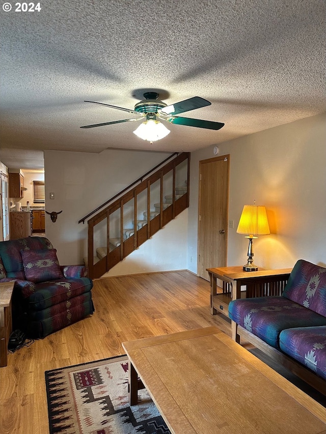 living room featuring hardwood / wood-style flooring, ceiling fan, and a textured ceiling