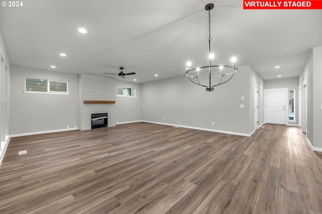 unfurnished living room with a large fireplace, wood-type flooring, and ceiling fan with notable chandelier