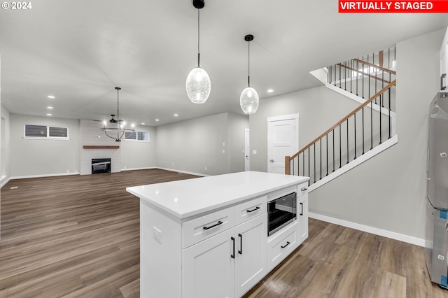 kitchen featuring hardwood / wood-style flooring, black microwave, a large fireplace, a center island, and white cabinets