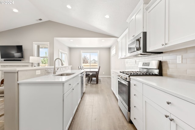 kitchen with sink, white cabinetry, appliances with stainless steel finishes, and vaulted ceiling