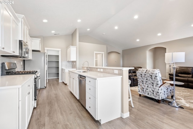 kitchen with appliances with stainless steel finishes, sink, white cabinetry, decorative backsplash, and lofted ceiling