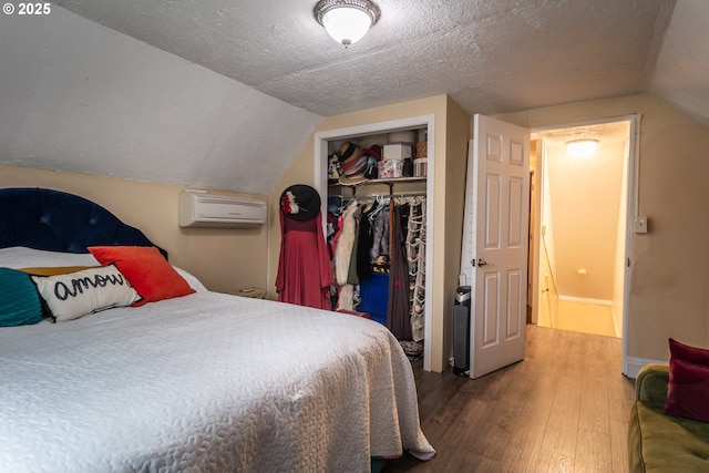 bedroom featuring a wall mounted air conditioner, wood-type flooring, lofted ceiling, a textured ceiling, and a closet