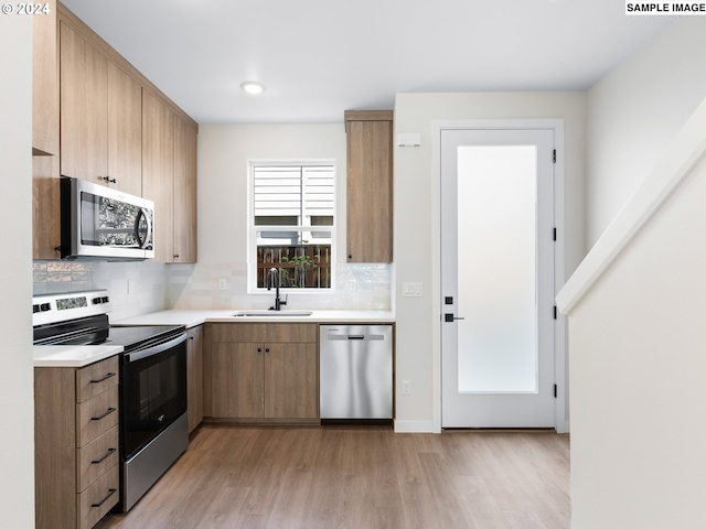 kitchen featuring appliances with stainless steel finishes, sink, decorative backsplash, and light hardwood / wood-style flooring