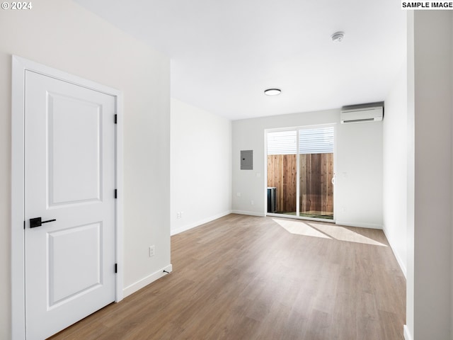 empty room featuring electric panel, light wood-type flooring, and a wall mounted air conditioner