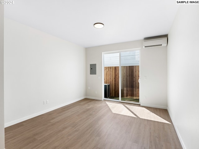 spare room with a wall unit AC, electric panel, and hardwood / wood-style floors