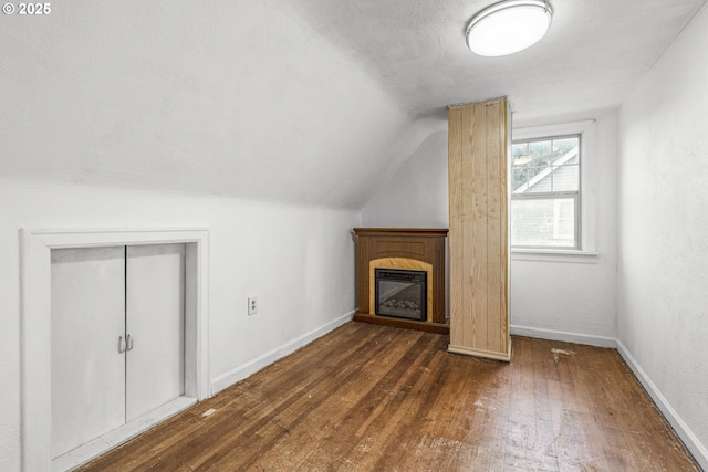 unfurnished living room with baseboards, dark wood finished floors, a glass covered fireplace, vaulted ceiling, and a textured ceiling