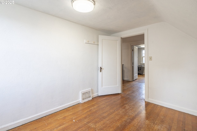 spare room with baseboards, visible vents, dark wood-type flooring, vaulted ceiling, and a textured ceiling