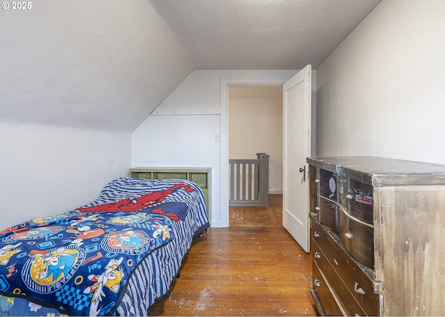 bedroom with dark wood-style floors, vaulted ceiling, and a textured ceiling