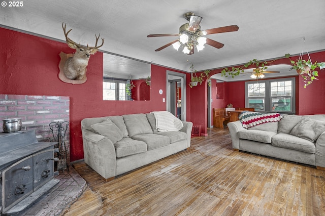 living area with a ceiling fan, a wood stove, and wood finished floors