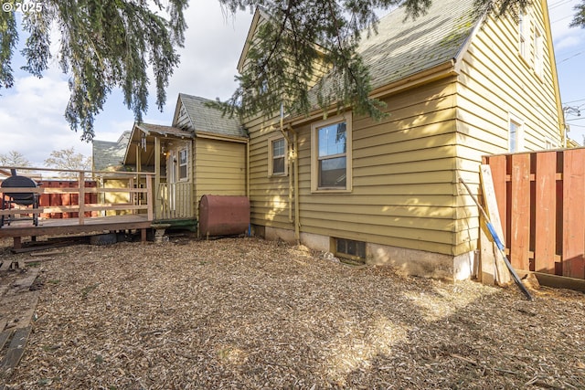 rear view of house featuring a deck, roof with shingles, fence, and heating fuel