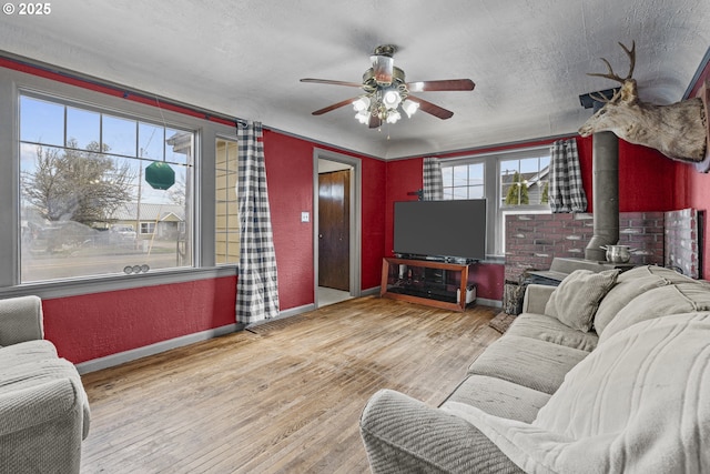 living area featuring baseboards, a textured wall, a wood stove, a textured ceiling, and light wood-style floors