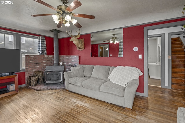 living area with baseboards, hardwood / wood-style floors, a wood stove, stairs, and a textured ceiling