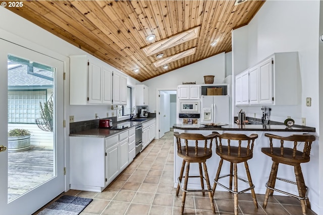 kitchen featuring white appliances, white cabinetry, lofted ceiling with skylight, and wood ceiling