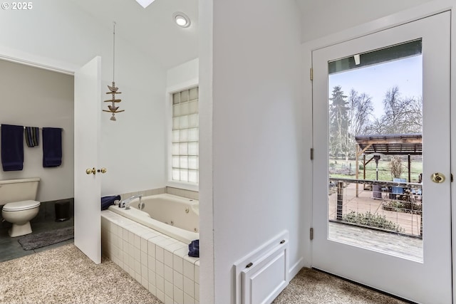 bathroom with plenty of natural light, tiled bath, and toilet