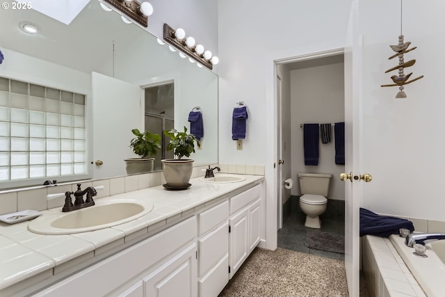 bathroom with a skylight, tiled bath, vanity, and toilet