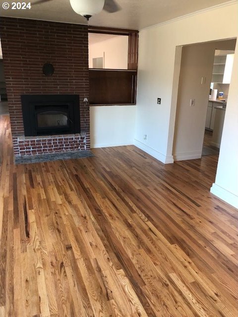 unfurnished living room with ornamental molding, hardwood / wood-style flooring, and a brick fireplace