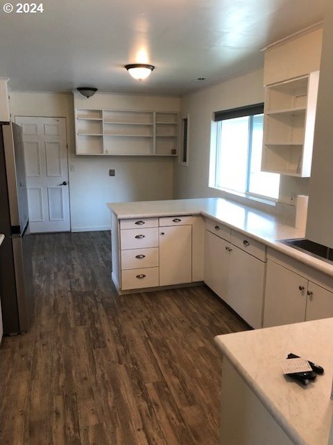 kitchen with dark wood-type flooring, kitchen peninsula, stainless steel fridge, and white cabinetry