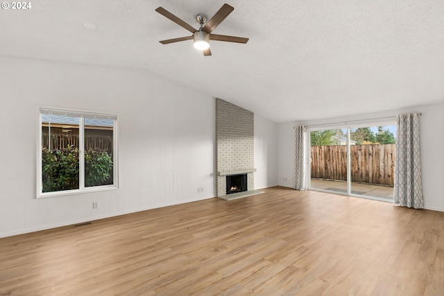 unfurnished living room with lofted ceiling, a brick fireplace, light hardwood / wood-style flooring, ceiling fan, and a textured ceiling