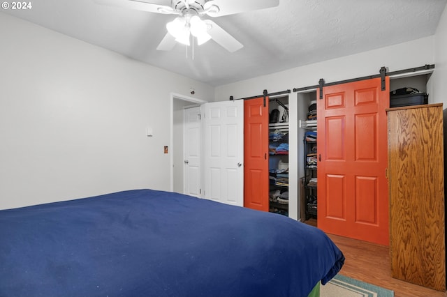 bedroom with a closet, ceiling fan, hardwood / wood-style flooring, and a barn door