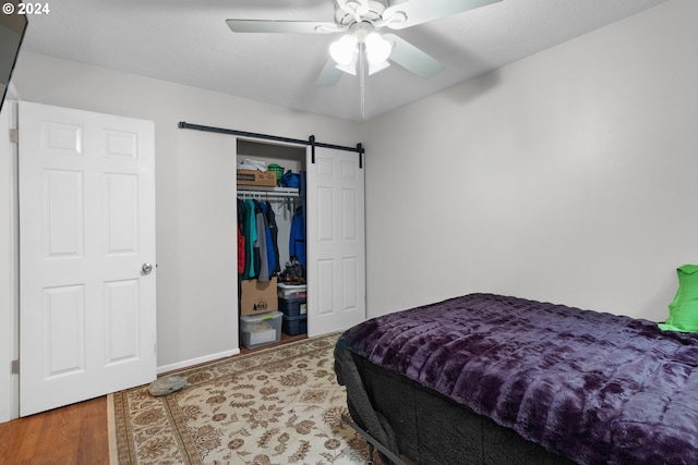 bedroom featuring hardwood / wood-style floors, a closet, ceiling fan, and a barn door