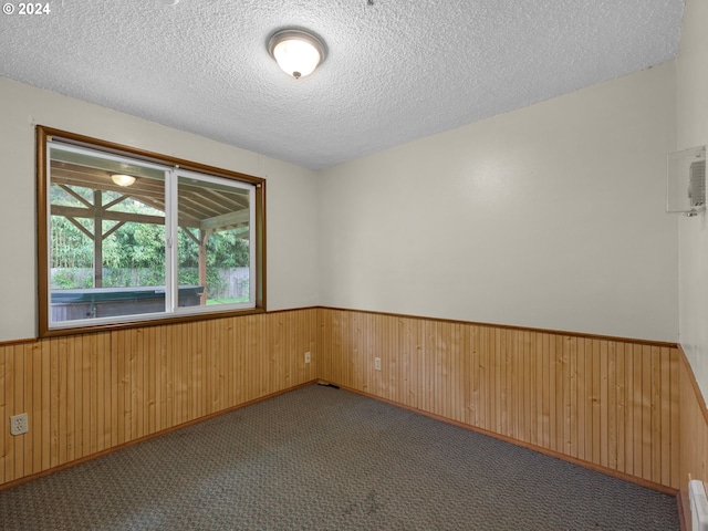 empty room featuring a textured ceiling, wooden walls, and dark carpet