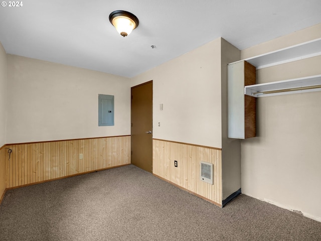 unfurnished bedroom featuring electric panel, a closet, wood walls, and carpet flooring