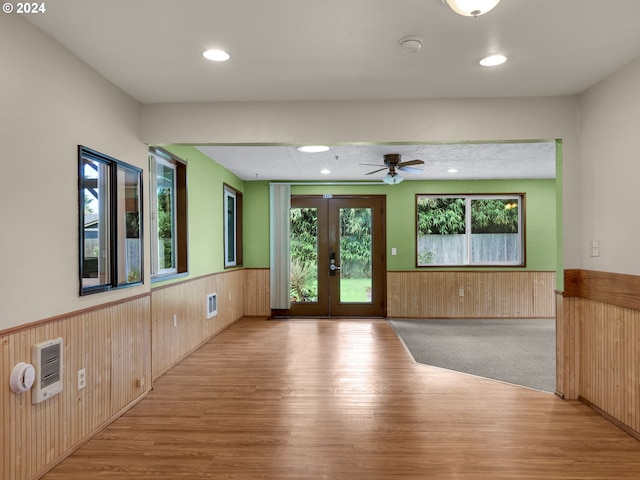 empty room featuring french doors, wooden walls, light wood-type flooring, and ceiling fan