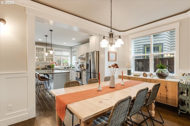 dining room with a notable chandelier, dark wood-style floors, ornamental molding, and a decorative wall