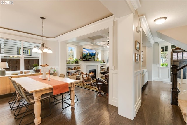 dining room featuring a lit fireplace, wainscoting, ceiling fan with notable chandelier, coffered ceiling, and dark wood-style flooring