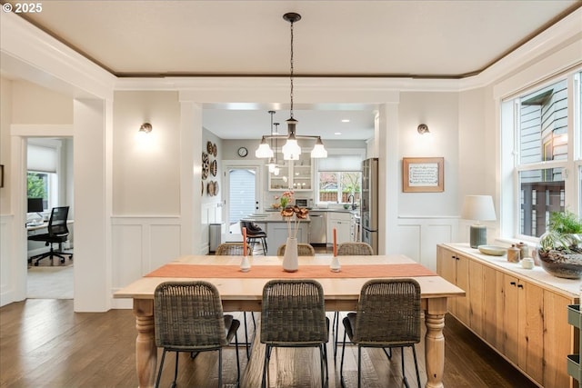 dining area featuring dark wood finished floors, a wainscoted wall, a decorative wall, and ornamental molding