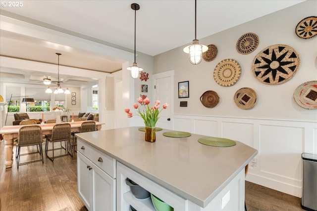 kitchen featuring dark wood-style flooring, light countertops, white cabinetry, decorative light fixtures, and a center island