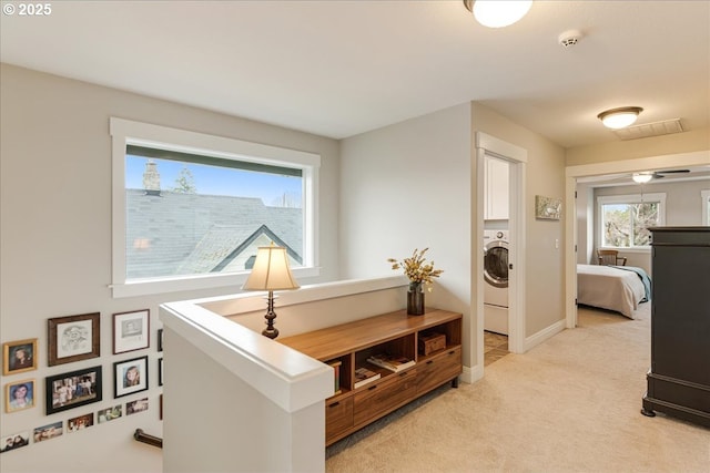 hall with washer / dryer, an upstairs landing, light colored carpet, and baseboards