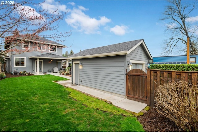 rear view of house with an outbuilding, a lawn, a gate, fence, and roof with shingles