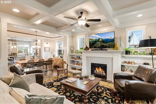 living area with beam ceiling, ceiling fan with notable chandelier, coffered ceiling, wood finished floors, and a fireplace