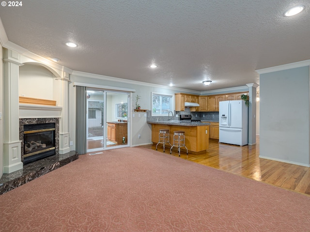 kitchen featuring white fridge with ice dispenser, kitchen peninsula, light wood-type flooring, a kitchen bar, and ornamental molding